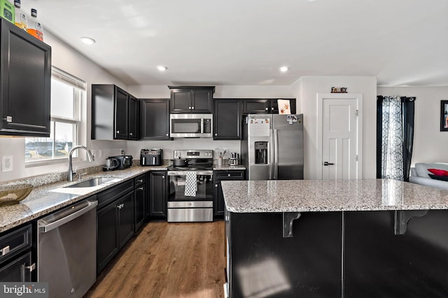 kitchen with stainless steel appliances, dark cabinetry, a breakfast bar area, and a sink