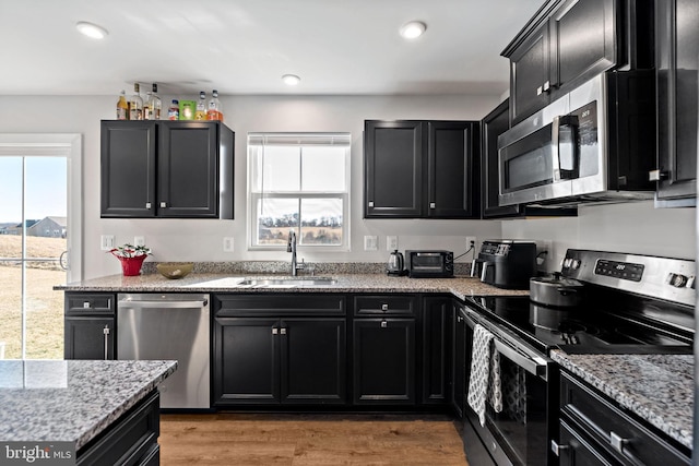 kitchen with stainless steel appliances, dark cabinetry, a sink, and light stone counters