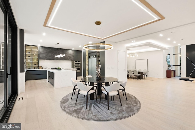 dining area featuring a tray ceiling, an inviting chandelier, light wood-style flooring, and recessed lighting