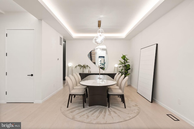 dining area with arched walkways, visible vents, baseboards, light wood-type flooring, and a tray ceiling