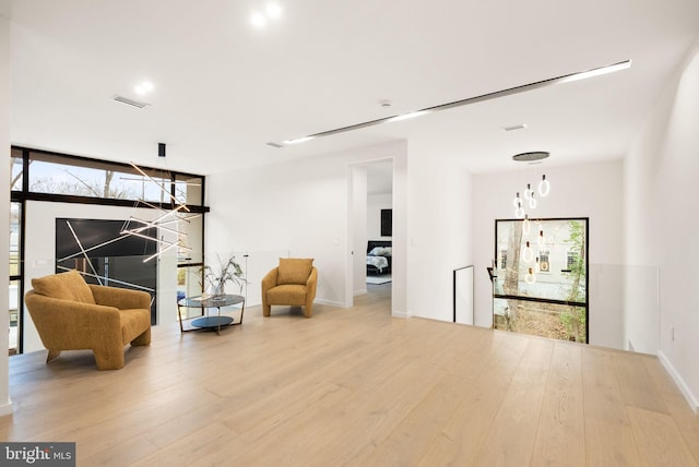 sitting room featuring expansive windows, visible vents, an upstairs landing, and wood finished floors