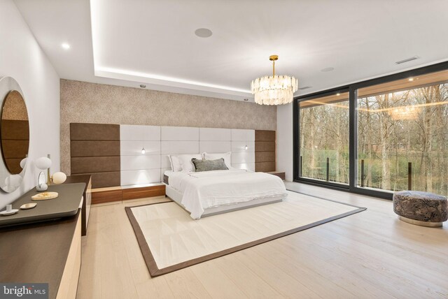 bedroom with visible vents, an inviting chandelier, an accent wall, expansive windows, and wood finished floors