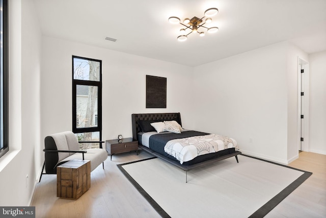 bedroom with light wood finished floors, visible vents, and baseboards