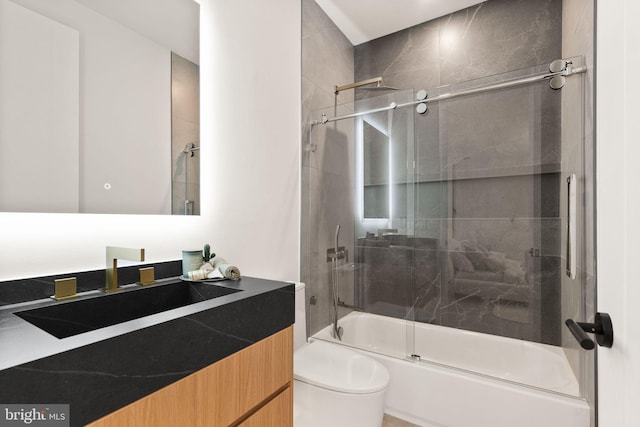 bathroom featuring toilet, combined bath / shower with glass door, and vanity