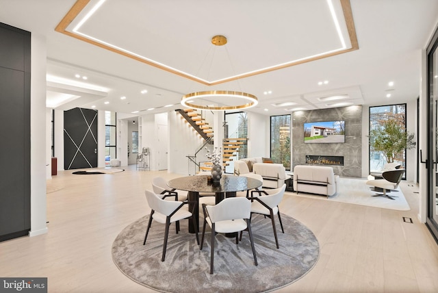 dining area with light wood finished floors, a raised ceiling, stairs, floor to ceiling windows, and a high end fireplace