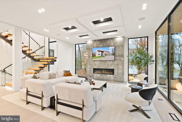 living room featuring coffered ceiling, a premium fireplace, stairway, wood finished floors, and expansive windows