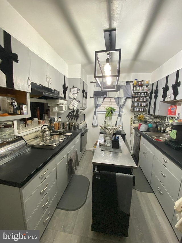 kitchen with dark countertops, a sink, oven, and under cabinet range hood