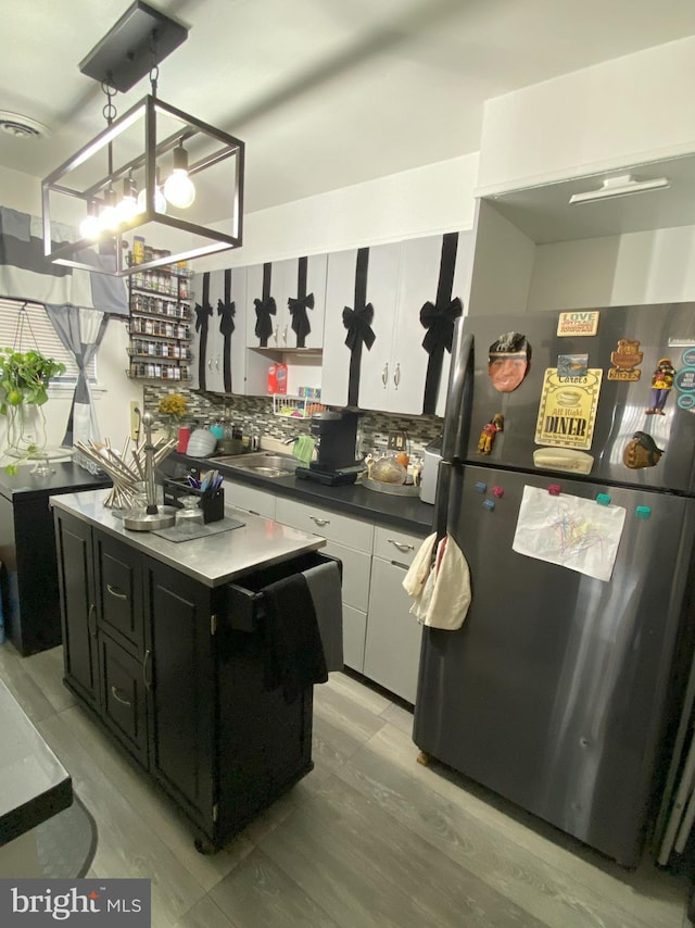 kitchen featuring tasteful backsplash, dark countertops, dark cabinets, freestanding refrigerator, and a sink