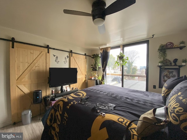 bedroom featuring ceiling fan, a barn door, access to outside, and wood finished floors