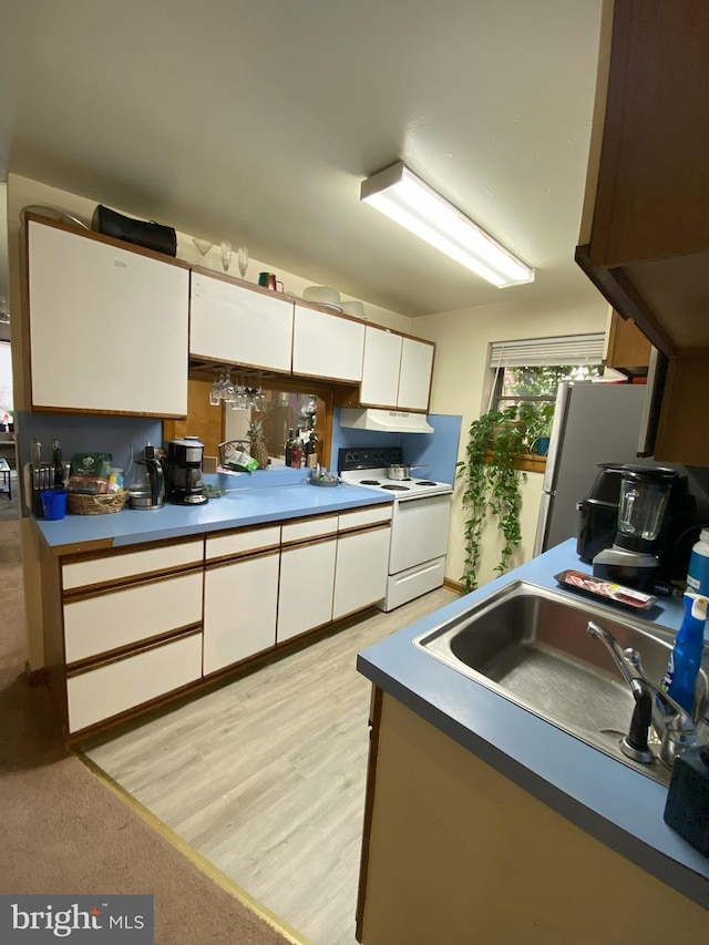 kitchen with electric range, white cabinets, freestanding refrigerator, under cabinet range hood, and a sink