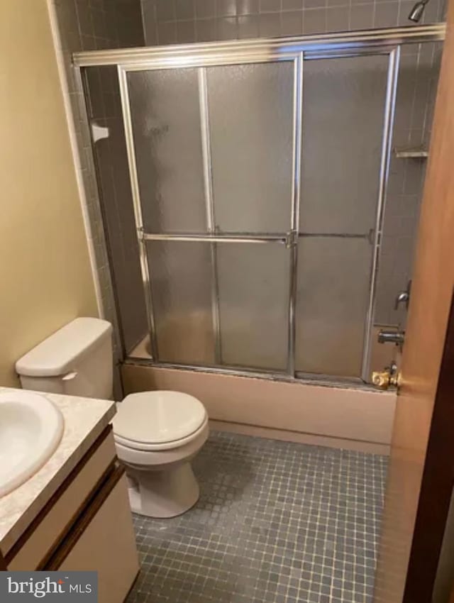 bathroom featuring toilet, tile patterned flooring, bath / shower combo with glass door, and vanity