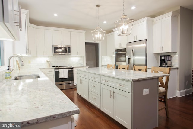 kitchen featuring appliances with stainless steel finishes, dark wood-type flooring, a sink, a kitchen island, and a kitchen breakfast bar