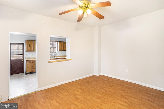 spare room featuring light wood finished floors, a ceiling fan, and baseboards