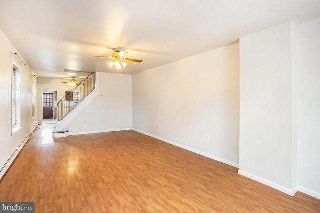 unfurnished living room featuring light wood-type flooring, a baseboard heating unit, baseboards, ceiling fan, and stairs