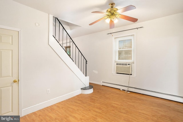 interior space with a ceiling fan, a baseboard heating unit, wood finished floors, stairway, and baseboards