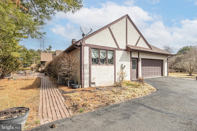 view of front of property with a shingled roof, stucco siding, a chimney, a garage, and driveway