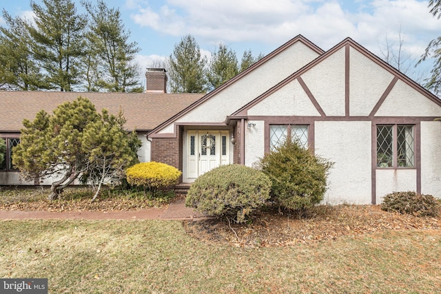 tudor home with stucco siding, a chimney, a front yard, and a shingled roof