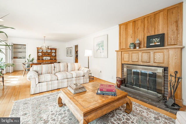 living room with light wood-type flooring, a fireplace with flush hearth, an inviting chandelier, and crown molding