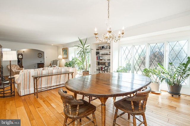 dining area with arched walkways, light wood-style floors, a chandelier, and crown molding