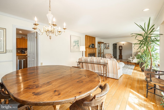 dining room featuring a fireplace, light wood-style floors, arched walkways, and ornamental molding