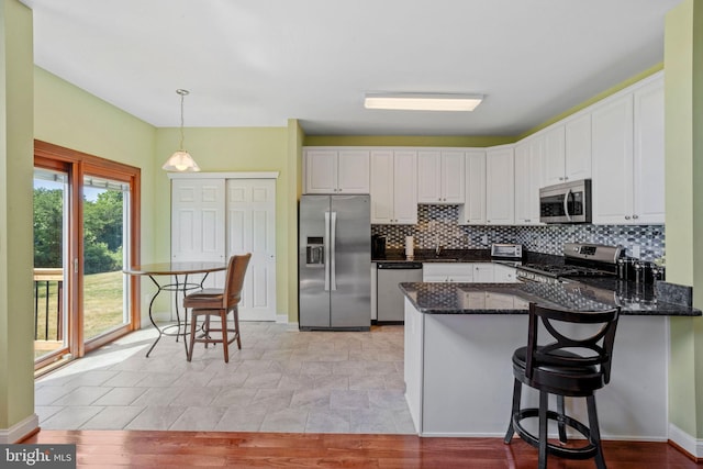 kitchen with stainless steel appliances, decorative backsplash, white cabinetry, dark stone countertops, and a peninsula