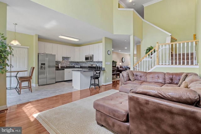 living area featuring stairs, baseboards, light wood-style flooring, and crown molding