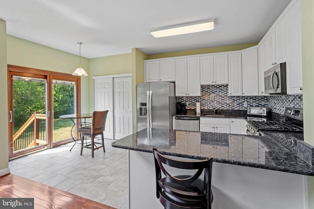 kitchen featuring a peninsula, white cabinets, appliances with stainless steel finishes, decorative backsplash, and pendant lighting