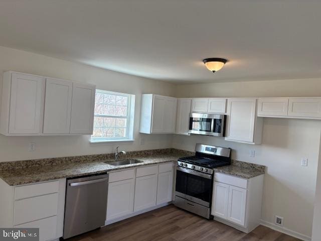 kitchen with dark wood-type flooring, a sink, stone countertops, white cabinetry, and stainless steel appliances