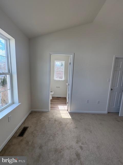 carpeted empty room with visible vents, baseboards, and vaulted ceiling