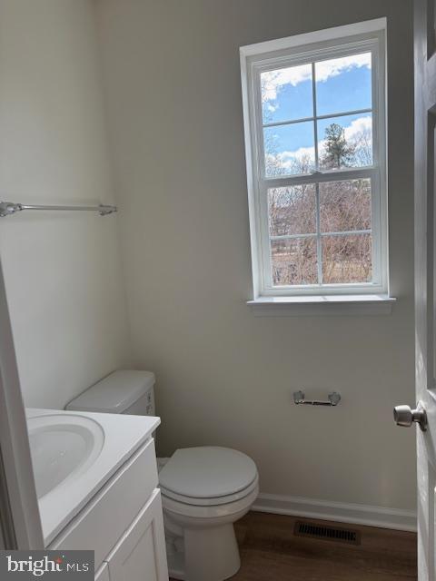 half bath with vanity, toilet, baseboards, and visible vents