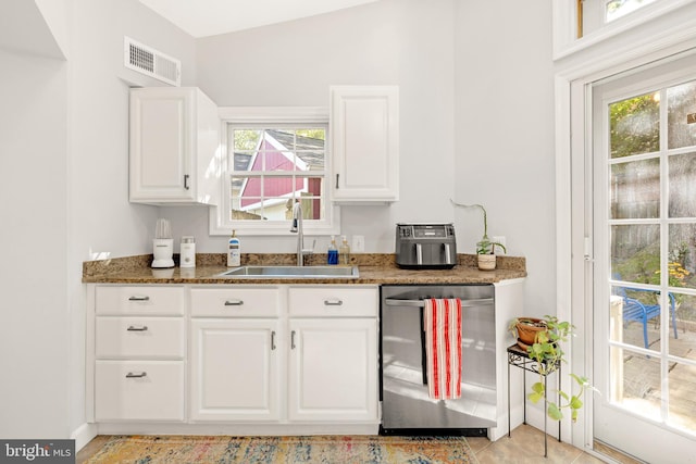 kitchen featuring visible vents, stainless steel dishwasher, white cabinets, a sink, and dark stone countertops