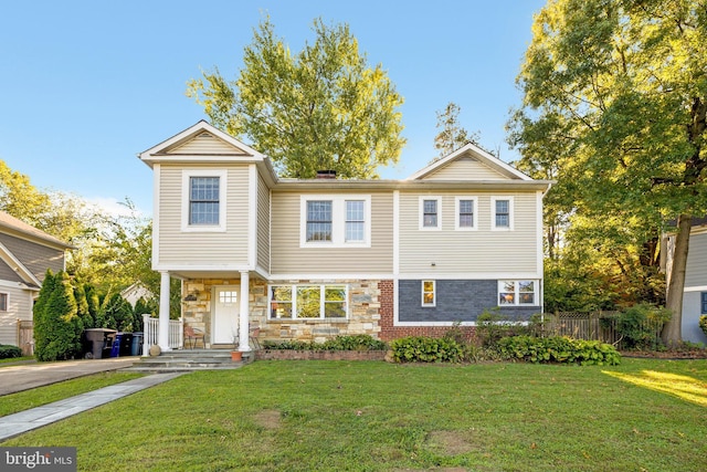 view of front of house featuring stone siding, brick siding, fence, and a front lawn