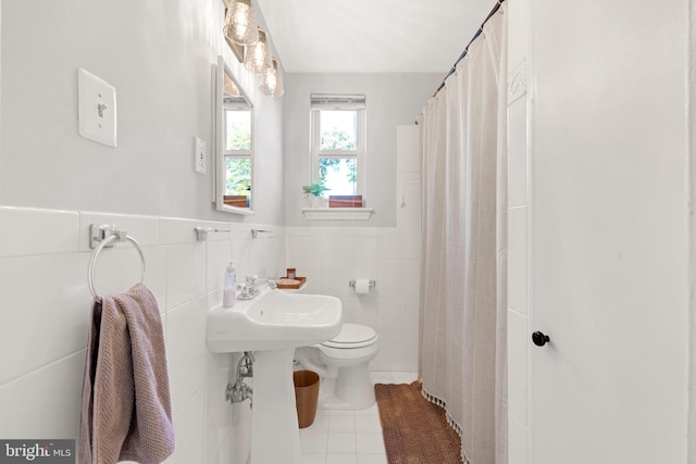 bathroom with toilet, a wainscoted wall, a shower with curtain, tile patterned flooring, and tile walls