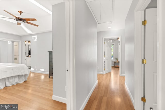 corridor with baseboards, attic access, and light wood-style floors