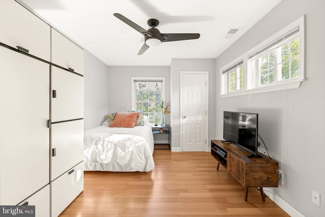 bedroom featuring a ceiling fan, baseboards, multiple windows, and light wood finished floors