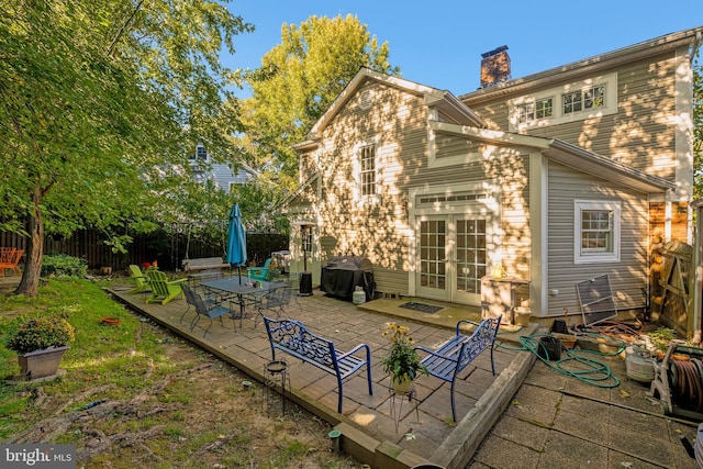 rear view of house with french doors, a patio area, fence, and a chimney