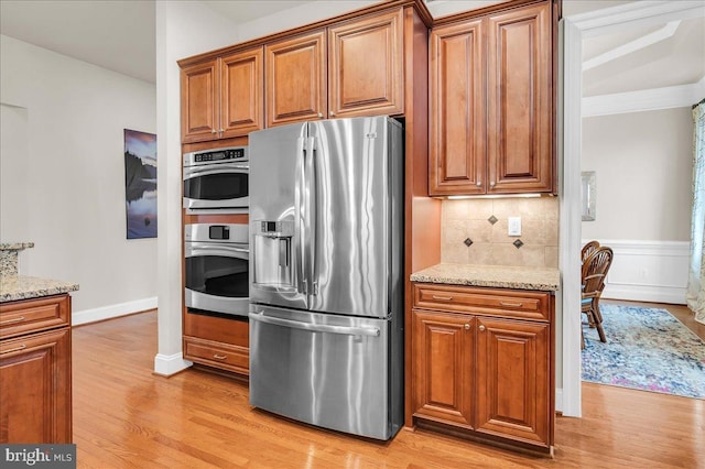 kitchen featuring appliances with stainless steel finishes, brown cabinetry, light wood-style flooring, and light stone countertops