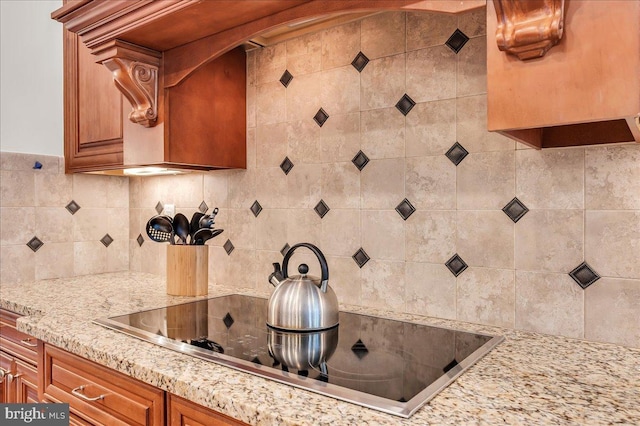 kitchen featuring light stone countertops, black electric cooktop, backsplash, and brown cabinetry