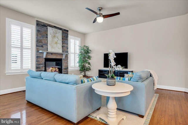 living room featuring baseboards, a stone fireplace, hardwood / wood-style flooring, and a ceiling fan