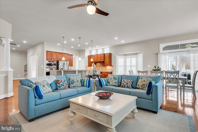 living room featuring ceiling fan, light wood finished floors, and ornate columns