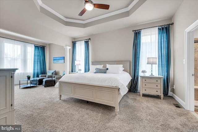 bedroom with a tray ceiling, multiple windows, and decorative columns