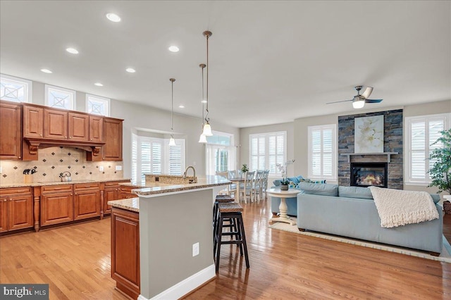 kitchen featuring brown cabinets, a breakfast bar area, decorative backsplash, light stone countertops, and light wood-type flooring