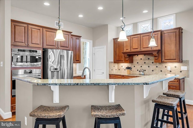 kitchen featuring stainless steel fridge, visible vents, brown cabinetry, a kitchen bar, and backsplash