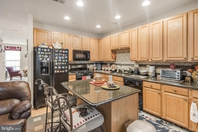 kitchen with black appliances, a toaster, light brown cabinets, and a kitchen breakfast bar