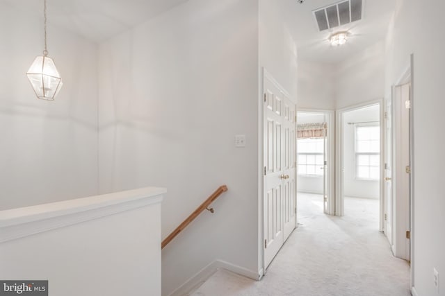 corridor with an upstairs landing and light carpet