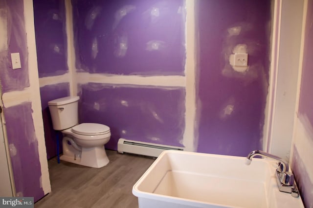 bathroom with wood finished floors, toilet, a sink, a bath, and baseboard heating