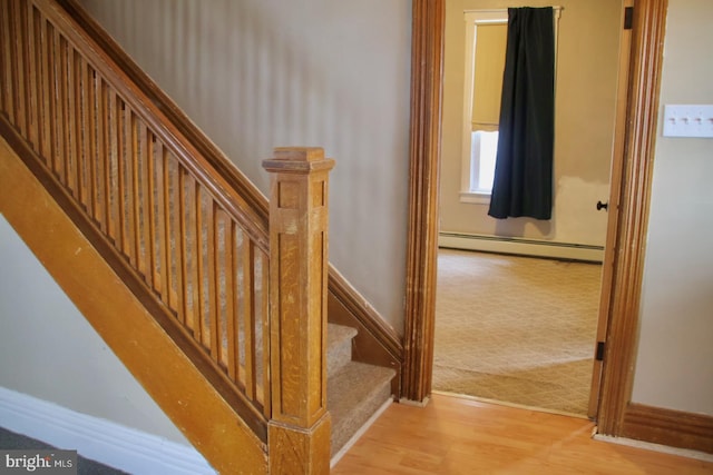 stairway with a baseboard radiator, baseboards, carpet floors, and wood finished floors