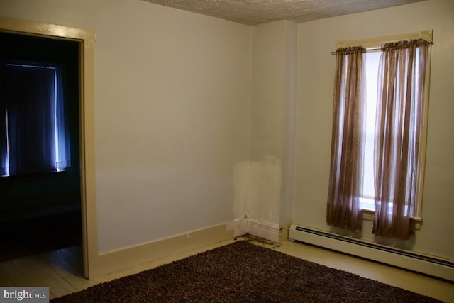 spare room with baseboard heating, a textured ceiling, and baseboards