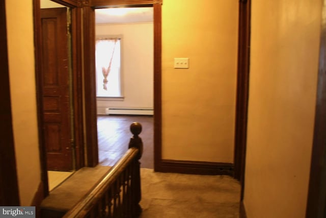 hallway featuring a baseboard heating unit, carpet, and baseboards