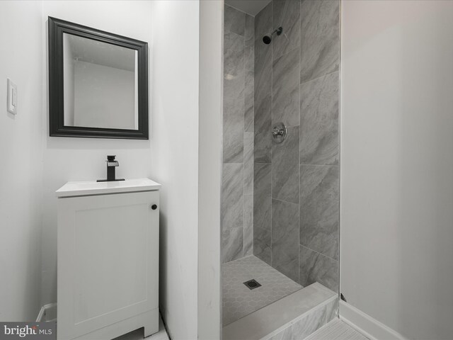 bathroom with baseboards, vanity, and a tile shower